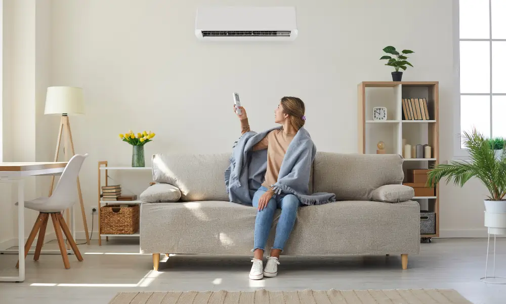 ブランケットをかけてソファに座り、HVACシステムを操作する女性。